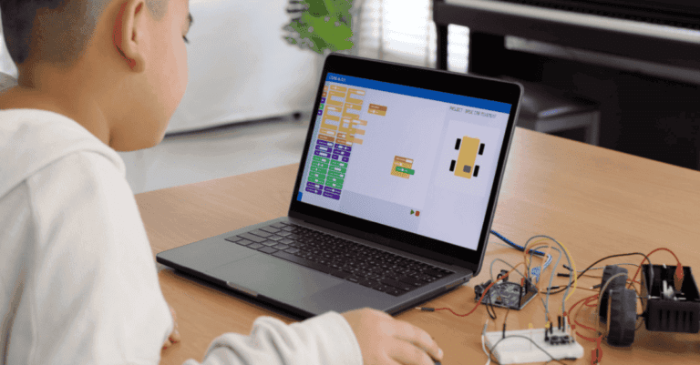 A child using a laptop to work on a coding project, with electronic components on a table.
