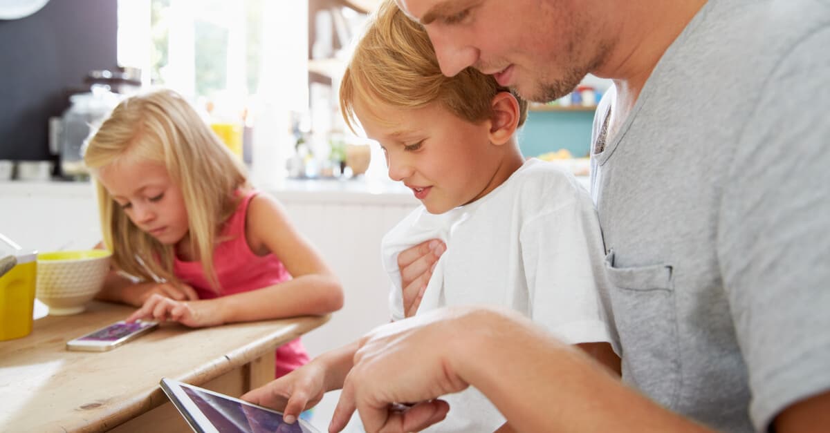 man holding boy using a tablet next to a girl using a mobile phone