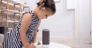 Young girl interacting with a smart speaker on a table.