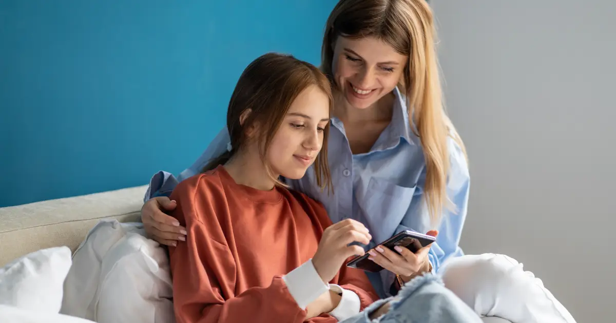 Parent and child sitting together on a sofa, looking at a smartphone.