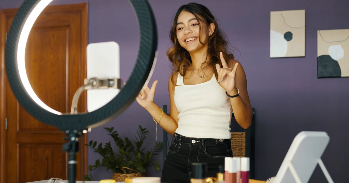 Teenager smiling and recording a video using a smartphone and ring light.