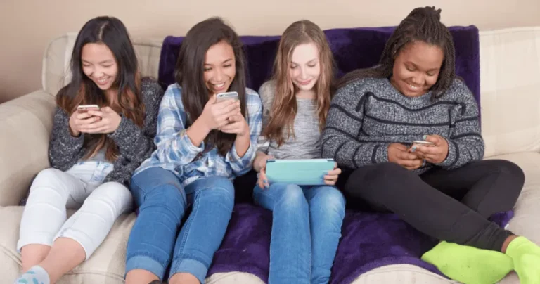 Four girls sitting on a sofa and playing with their devices