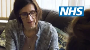 Женщина в очках разговаривает с кем-то. Тест читает "NHS"
