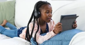 A young girl lies on her stomach using a tablet device.