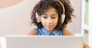 A young girl wears headphones while using her laptop.