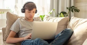 A boy uses a laptop on a sofa.