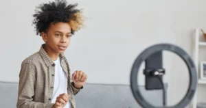 A pre-teen boy records himself dancing in front of his smartphone and a ring light.