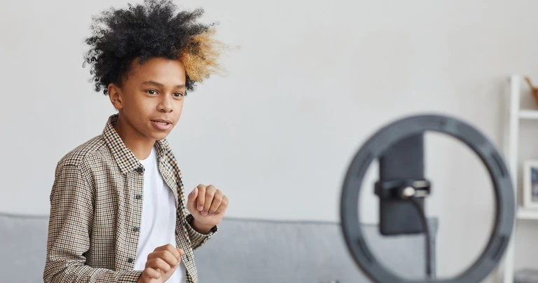 A pre-teen boy records himself dancing in front of his smartphone and a ring light.