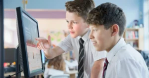 Two school boys look at a computer in school.