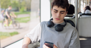 Boy on bus looking at phone sadly
