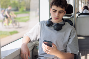Boy on bus looking at phone sadly