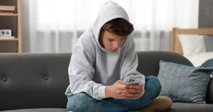 Menino triste sentado no sofá mexendo no celular