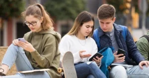 Three teens look at their smartphones with two discussing something they see.