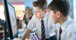 Two school boys look at a computer screen, talking.