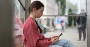 A girl sits outside using a smartphone.