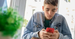 A young person uses their smartphone, possibly for social media, which is the main focus of the government's consultation.