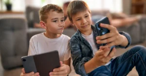 Two boys look at devices together.